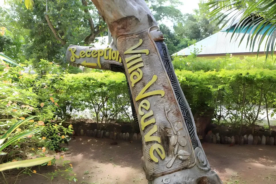 Ein geschnitztes Holzschild mit Reception und Villa Veuve in einer grünen Hecke